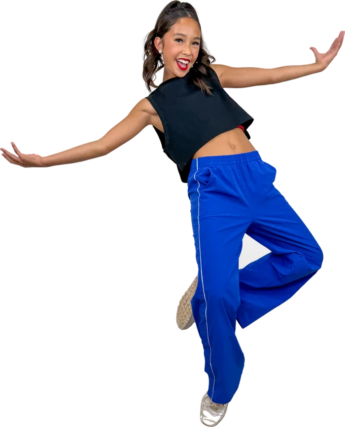 Tween dancer in blue trousers and a black crop top jumping with arms wide